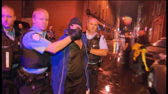 Un agent du SPVM remonte la cagoule du suspect sur son visage pendant que ce denrier vocifère des propos incompréhensibles aux journalistes. Un agent du SPVM remonte la cagoule du suspect sur son visage pendant que ce denrier vocifère des propos incompréhensibles aux journalistes.