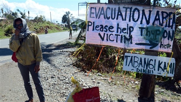 Un Philippin attend devant une affiche qui annonce un centre d'accueil pour les sinistrés du typhon Bopha Un Philippin attend devant une affiche qui annonce un centre d'accueil pour les sinistrés du typhon Bopha
