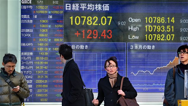 Des Japonais marchent devant un écran montrant les cours de la bourse, alors que le gouvernement vient d'annoncer une plan de relance économique Des Japonais marchent devant un écran montrant les cours de la bourse, alors que le gouvernement vient d'annoncer une plan de relance économique