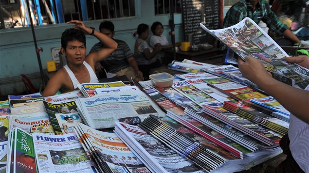 Devant un kiosque à journaux, un homme tient une copie du Voice daily, version quotidienne du magazine privé Voice, publié de façon hebdomadaire avant lundi. Photo prise au Myanmar le 1er avril 2013. Devant un kiosque à journaux, un homme tient une copie du Voice daily, version quotidienne du magazine privé Voice, publié de façon hebdomadaire avant lundi. Photo prise au Myanmar le 1er avril 2013.