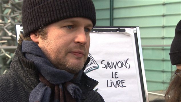 L'auteur et éditeur Tristan Malavoy-Racine devant l'affiche « Sauvons les livres » dessinée par l'illustrateur Jacques Goldstyn. L'auteur et éditeur Tristan Malavoy-Racine devant l'affiche « Sauvons les livres » dessinée par l'illustrateur Jacques Goldstyn.