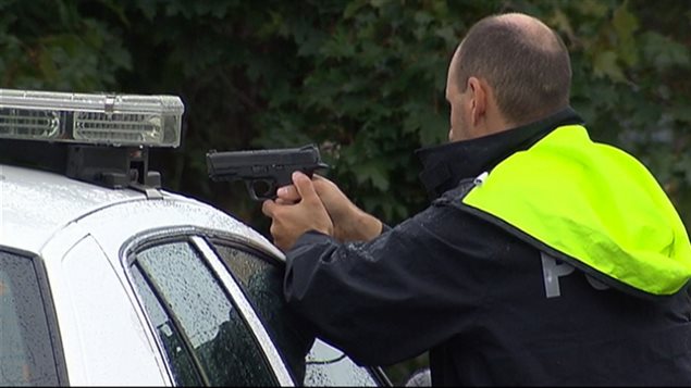 Un policier pointe son arme ver la demeure où le suspect demeurait terré. Un policier pointe son arme ver la demeure où le suspect demeurait terré.