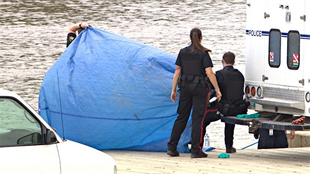 Les policiers ont recouvert d'une toile le corps d'une femme repêché dans la rivière Rouge, près du quai Alexander, le 17 août. Les policiers ont recouvert d'une toile le corps d'une femme repêché dans la rivière Rouge, près du quai Alexander, le 17 août.