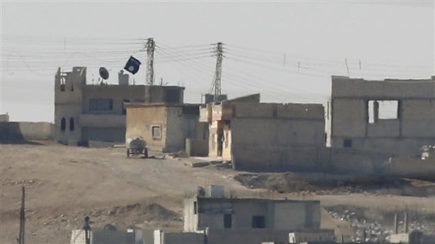 Un drapeau de l'État islamique flotte sur un bâtiment de Kobané. Un drapeau de l'État islamique flotte sur un bâtiment de Kobané.