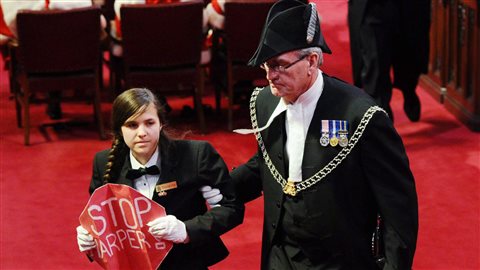 Le sergent d'armes Kevin Vickers escorte la jeune page Brigette DePape hors du Sénat, alors que le gouverneur général David Johnston livre le discours du Trône. Le sergent d'armes Kevin Vickers escorte la jeune page Brigette DePape hors du Sénat, alors que le gouverneur général David Johnston livre le discours du Trône.