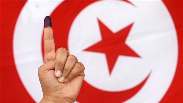 Une Tunisienne montre son doigt taché d'encre devant un drapeau du pays, après avoir voté. Une Tunisienne montre son doigt taché d'encre devant un drapeau du pays, après avoir voté.