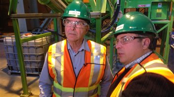 Jean-Claude Savoie (à gauche) et Chris Hooper dans une usine. Ils portent des dossars oranges et jaunes et un casque vert. Ils portent aussi des lunettes de sécurité. Jean-Claude Savoie (à gauche) et Chris Hooper dans une usine. Ils portent des dossars oranges et jaunes et un casque vert. Ils portent aussi des lunettes de sécurité.