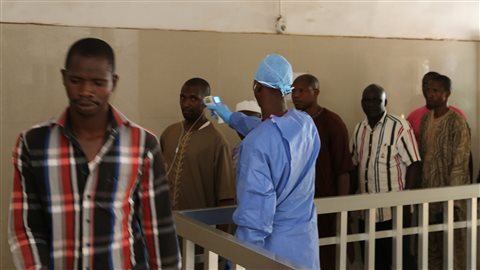 Un membre du personnel d'un hôpital de Conakry prend la température de personnes qui pourraient être infectées par le virus Ebola Un membre du personnel d'un hôpital de Conakry prend la température de personnes qui pourraient être infectées par le virus Ebola