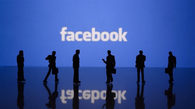 Des silhouettes sombres se tiennent devant le logo du réseau social Facebook. Des silhouettes sombres se tiennent devant le logo du réseau social Facebook.