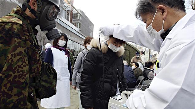 Un médecin vérifie le taux de radiation d'une femme sous le regard d'un militaire, dans la préfecture de Fukushima. Un médecin vérifie le taux de radiation d'une femme sous le regard d'un militaire, dans la préfecture de Fukushima.