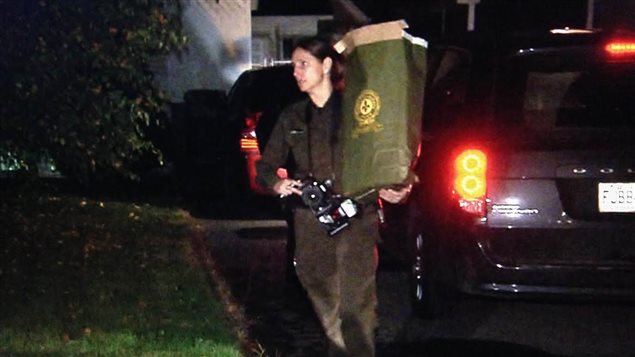 Une policière quitte la maison du suspect abattu avec un sac de documents. Une policière quitte la maison du suspect abattu avec un sac de documents.
