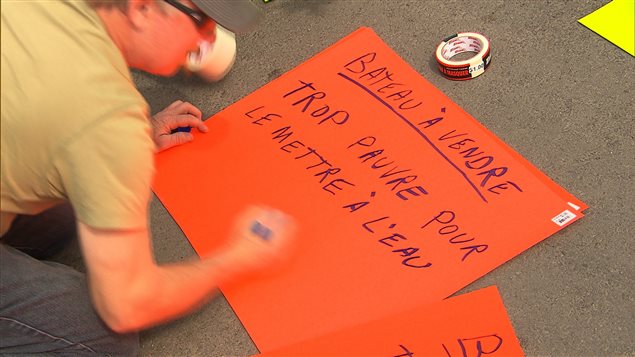 Un homme prépare une pancarte pour montrer son mécontentement face aux hausses des tarifs pour les rampes de mises à l'eau des municipalités. Un homme prépare une pancarte pour montrer son mécontentement face aux hausses des tarifs pour les rampes de mises à l'eau des municipalités.
