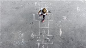 Une petite fille joue à la marelle dans une cour d'école 
