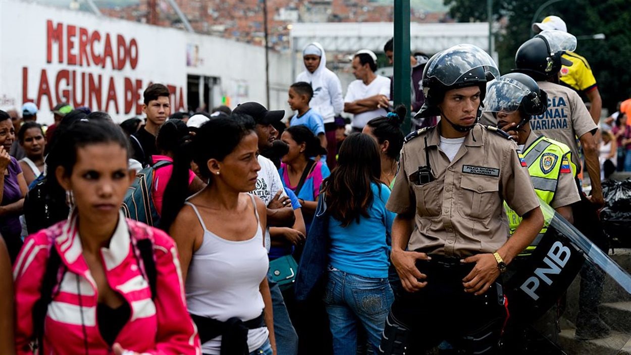 La police surveille les citoyens qui font la file pour acheter l'épicerie à Caracas, au Venezuela, le 11 juin 2016. La police surveille les citoyens qui font la file pour acheter l'épicerie à Caracas, au Venezuela, le 11 juin 2016.