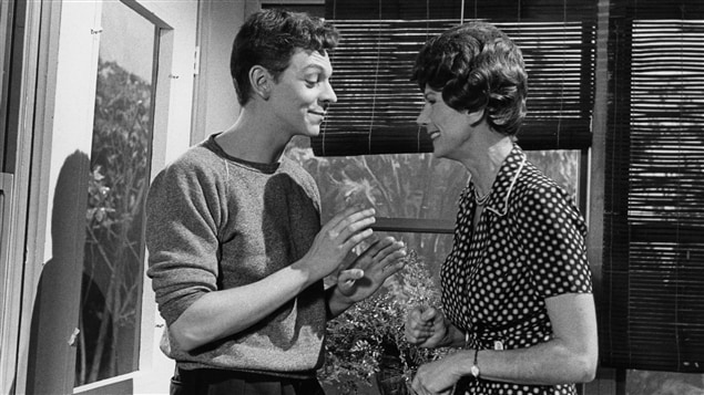 Dans la maison, Clovis Jobin (Marc Labrèche) est debout face à Mme Dessaules (Béatrice Picard) qui lui sourit. Dans la maison, Clovis Jobin (Marc Labrèche) est debout face à Mme Dessaules (Béatrice Picard) qui lui sourit.