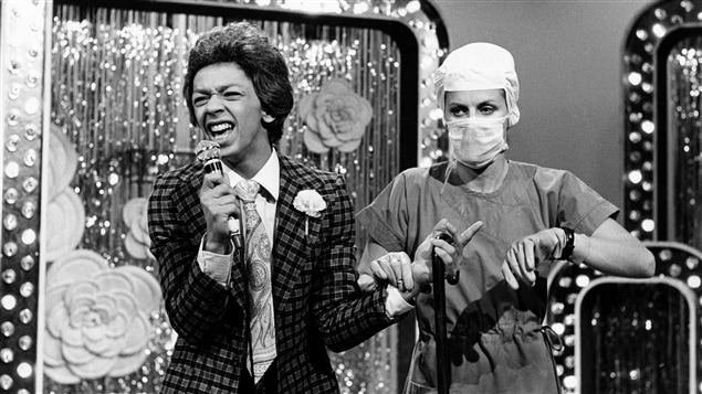Sur une scène, un chanteur crooner (Normand Brathwaite) est examiné par un docteur (Michèle Deslauriers). Sur une scène, un chanteur crooner (Normand Brathwaite) est examiné par un docteur (Michèle Deslauriers).