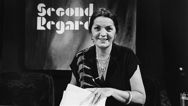 Dans un studio de télévision, l'animatrice Myra Cree, souriante, est assise à un bureau avec des documents dans les mains. Un écran en arrière-plan affiche le nom de l'émission. Dans un studio de télévision, l'animatrice Myra Cree, souriante, est assise à un bureau avec des documents dans les mains. Un écran en arrière-plan affiche le nom de l'émission.