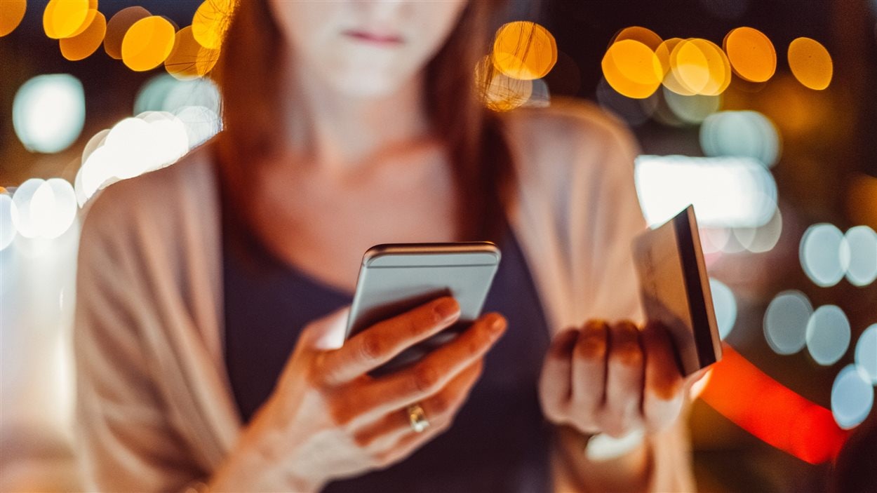 Une femme tient un cellulaire dans une main et une carte de crédit dans l'autre. Une femme tient un cellulaire dans une main et une carte de crédit dans l'autre.