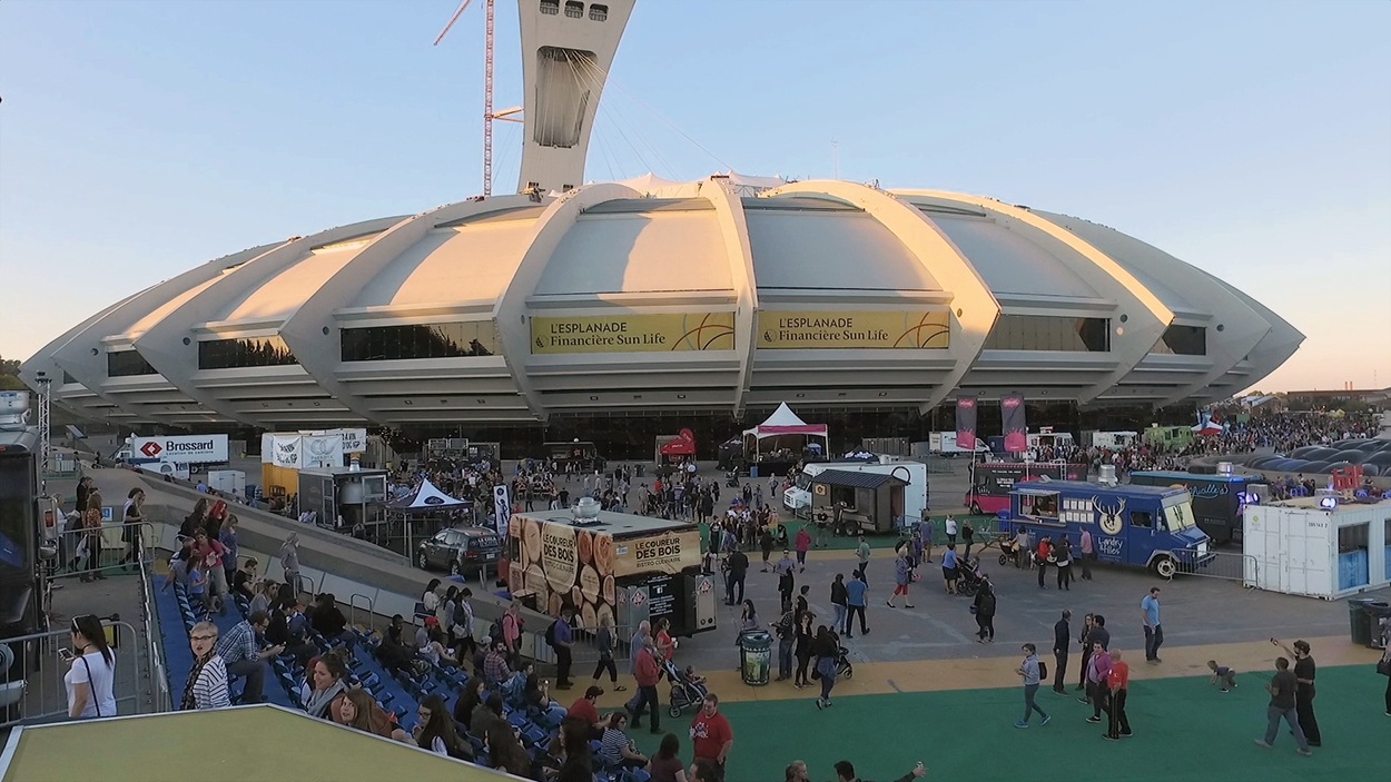 Avec le Stade olympique en arrière-plan, une vue d'ensemble de plusieurs camions de bouffe de rue stationnés sur l'esplanade.